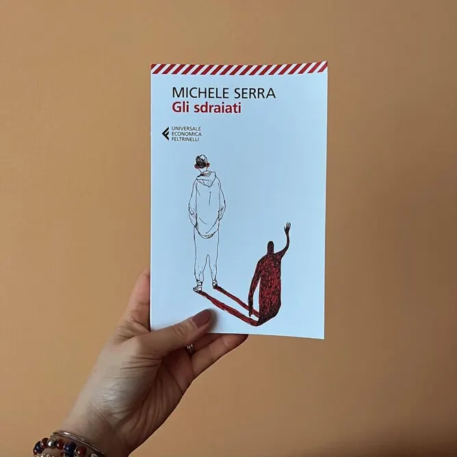 Una mano che tiene il libro "Gli sdraiati" di Michele Serra